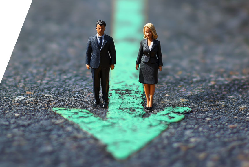 Zwei Miniaturfiguren stehen auf Asphalt und schauen den Besucher an. Ein türkisfarbener Pfeil ist auf den Asphalt gemalt. Er kommt aus der Unschärfe von oben und zeigt nach unten in Richtung des Betrachters.